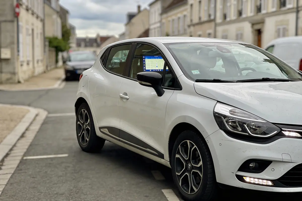 Voiture blanche moderne avec GPS visible, stationnée dans une rue résidentielle calme et pavée.