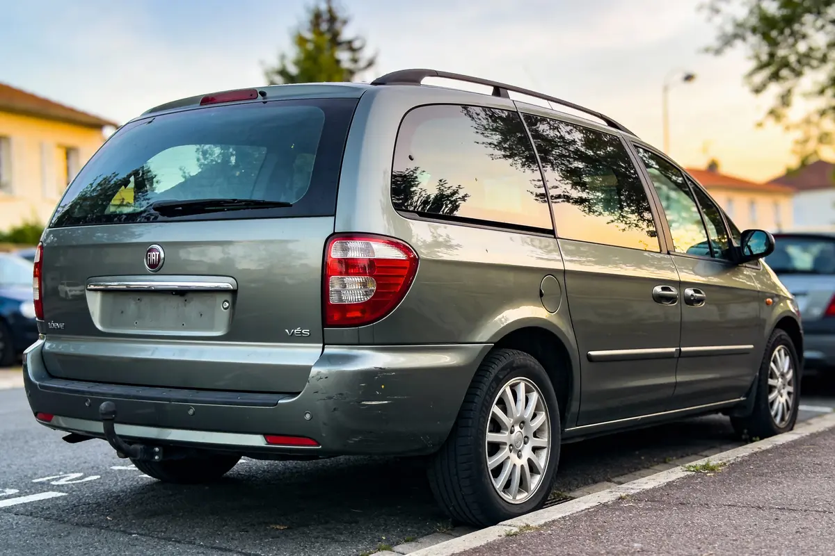 Monospace vert stationné dans la rue, près du trottoir, au crépuscule, reflet d'arbres sur les vitres.