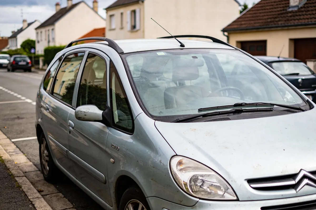Voiture argentée stationnée dans une rue résidentielle avec maisons en arrière-plan.