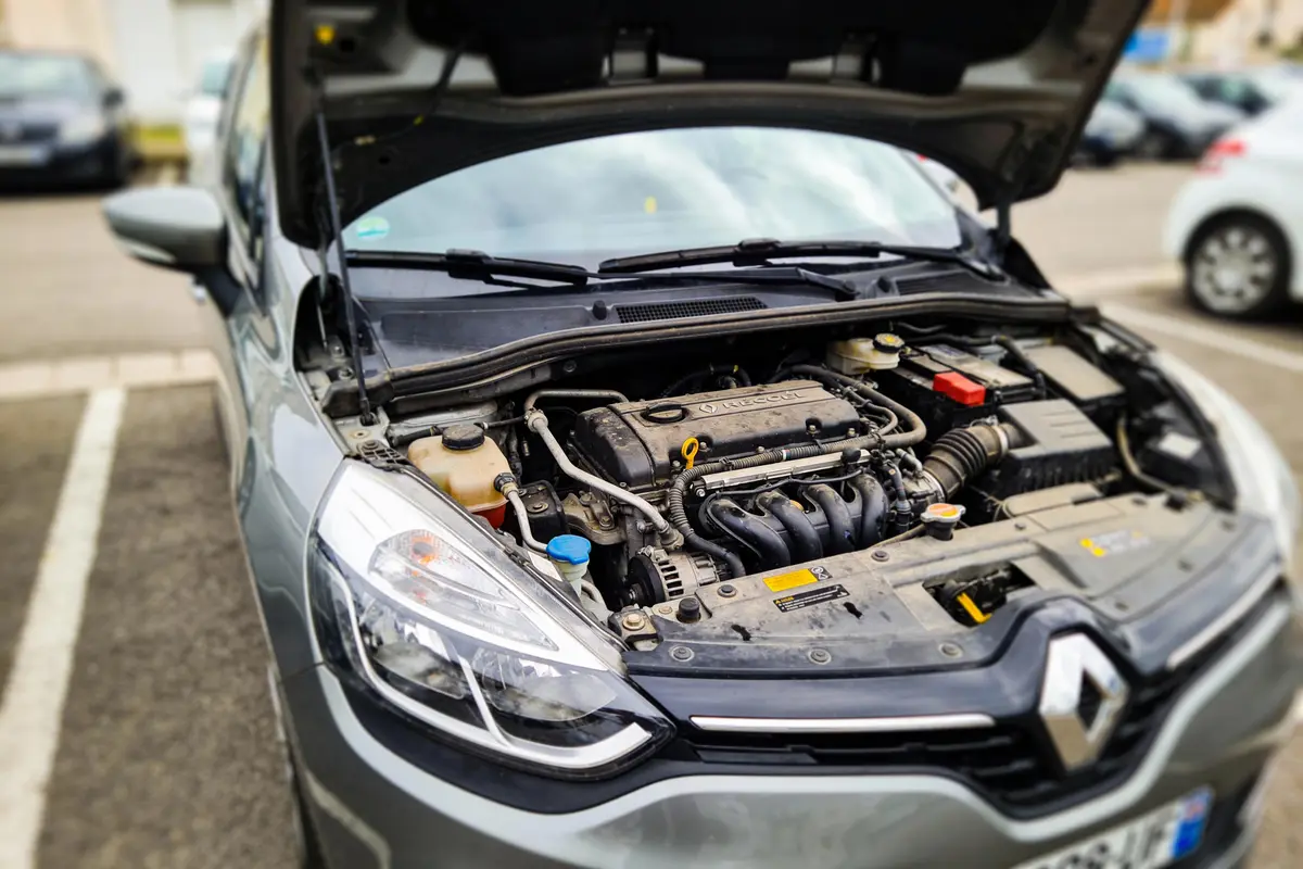 Capot ouvert d'une voiture Renault, montrant le moteur, garée près d'autres véhicules sur la route.