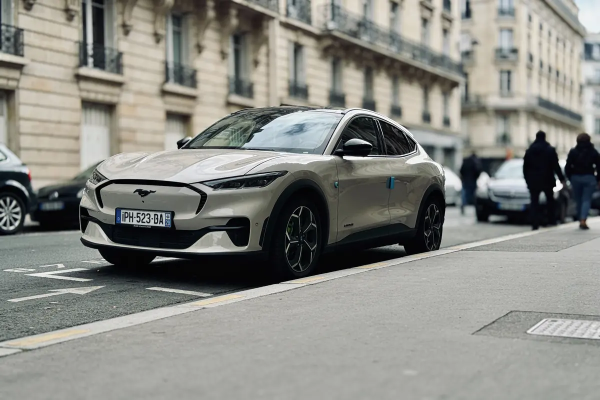 Voiture électrique stationnée dans une rue urbaine, devant un bâtiment classique. Passants flous en arrière-plan.