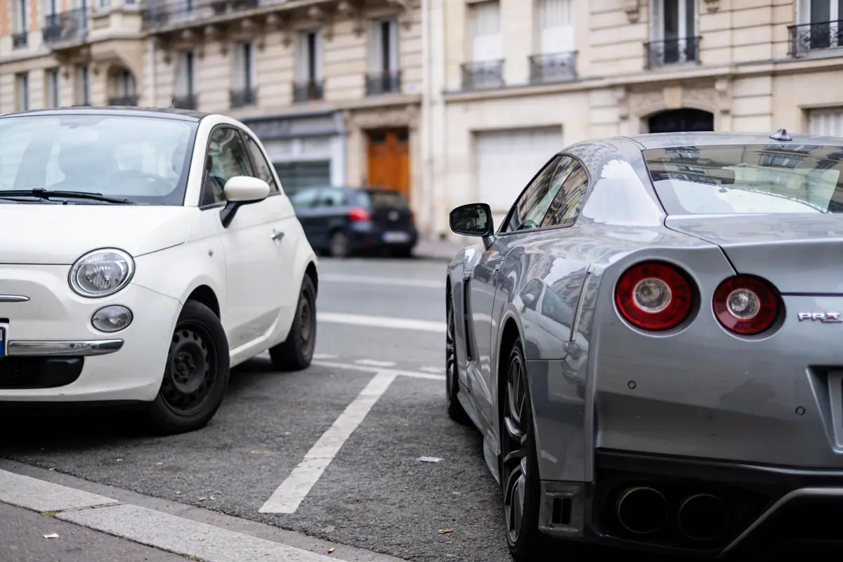 Voiture blanche et voiture grise garées côte à côte dans une rue urbaine, architecture en arrière-plan.