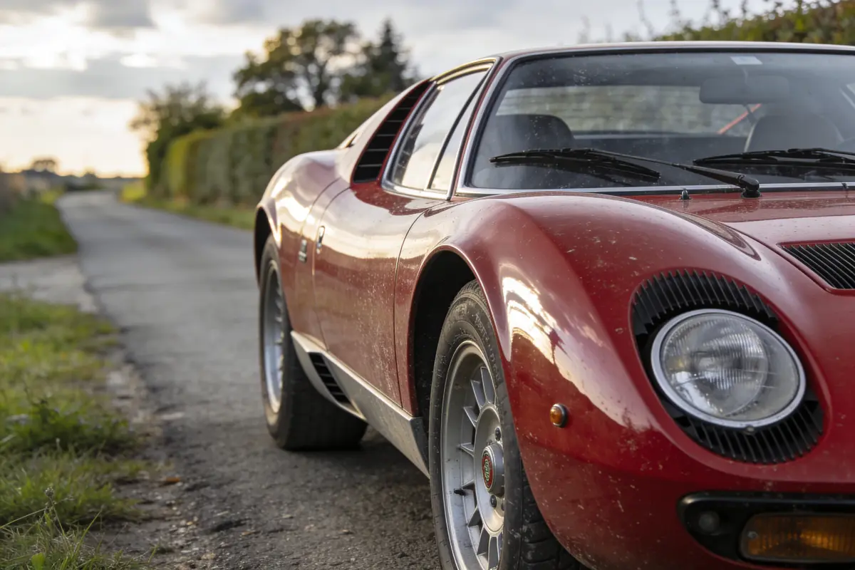 Voiture classique rouge sur une route de campagne, éclairée par une lumière de coucher de soleil.
