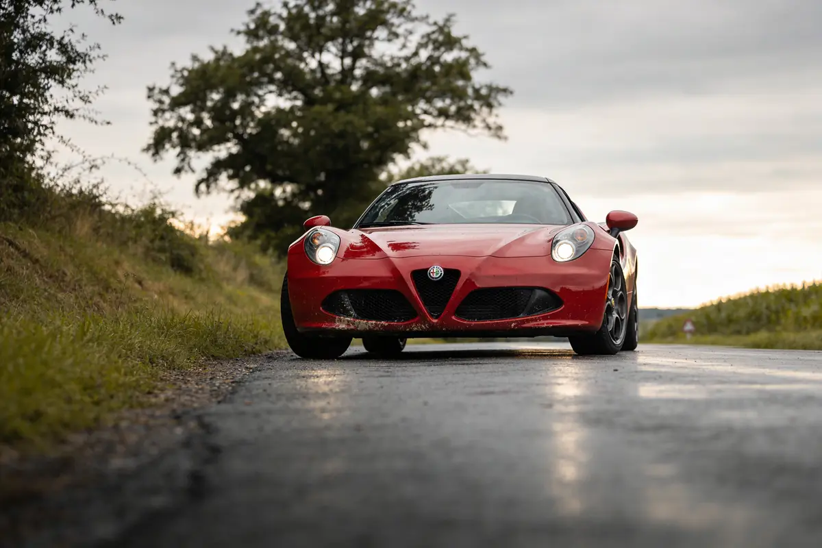 Voiture rouge sur route de campagne par temps nuageux, arbre en arrière-plan.