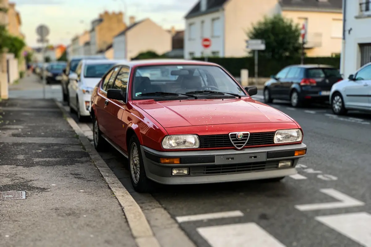 Voiture rouge Alfa Romeo garée dans une rue résidentielle avec d'autres véhicules alignés côte à côte.