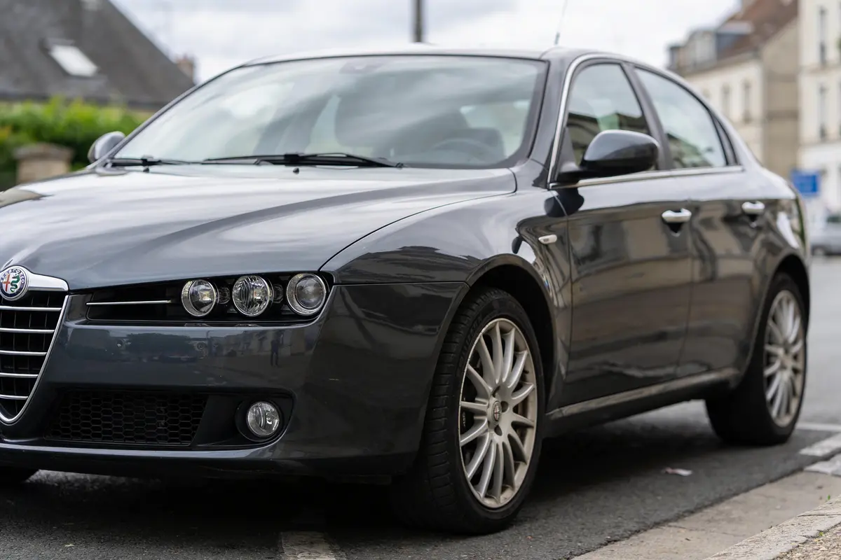 Voiture berline noire stationnée en extérieur, design sportif, jantes alliage, rue résidentielle, maisons floues en arrière-plan.