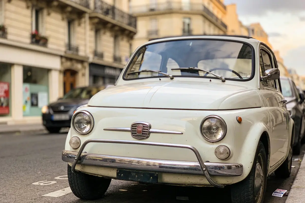 Petite voiture citadine blanche garée dans une rue avec des bâtiments en arrière-plan.