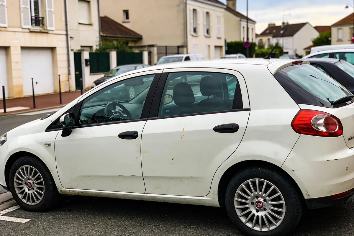 Voiture blanche Fiat garée dans une rue résidentielle avec maisons en arrière-plan.