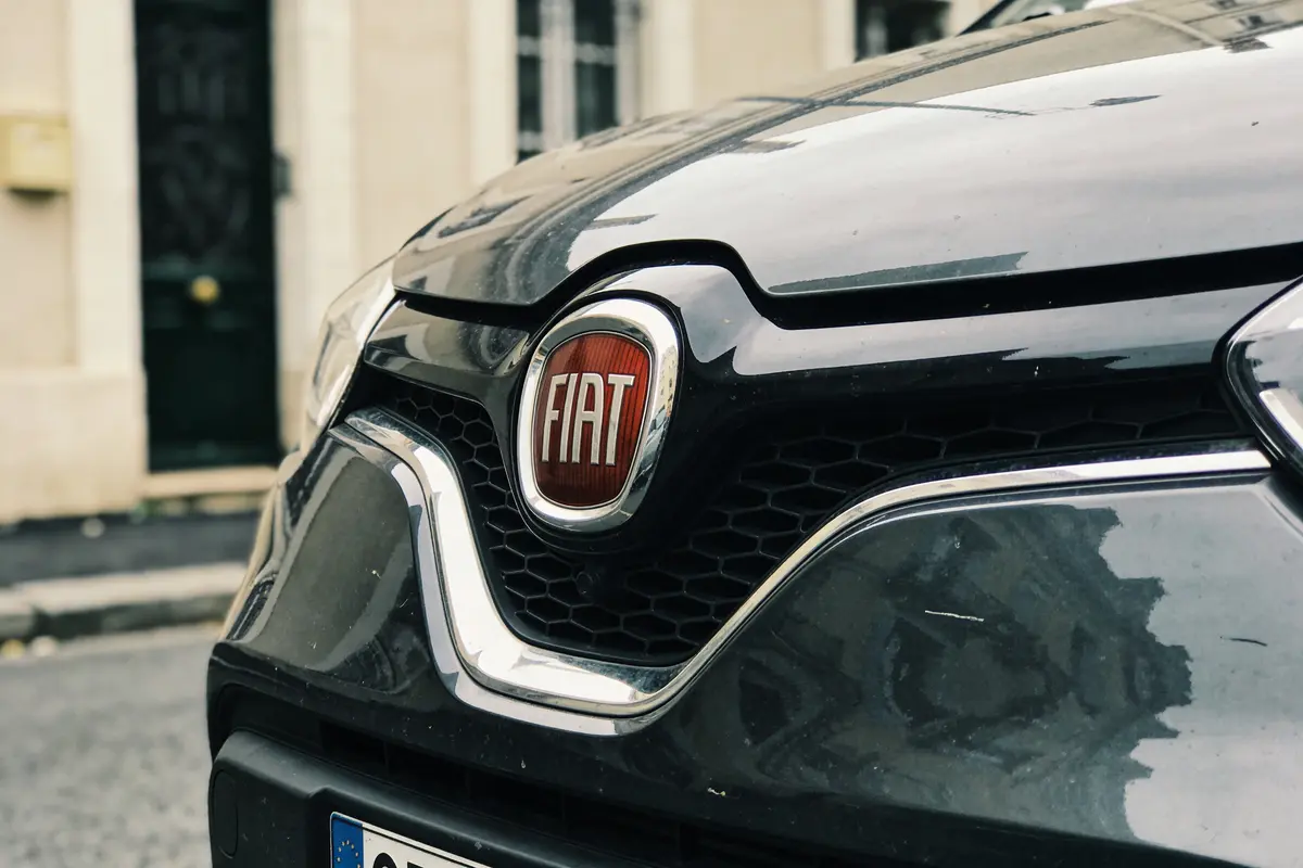 Gros plan sur le logo Fiat sur la calandre d'une voiture grise, rue en arrière-plan.