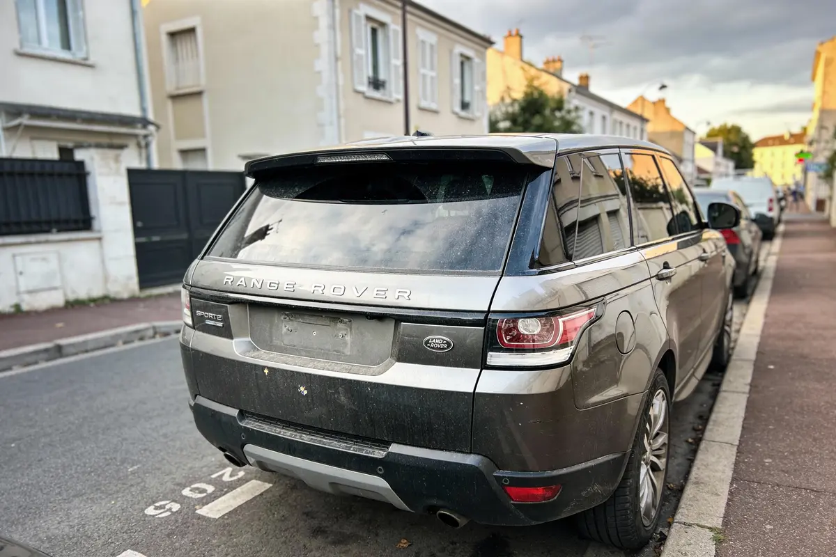 Land Rover gris garé dans une rue, maisons résidentielles en arrière-plan. Plaque d'immatriculation absente.