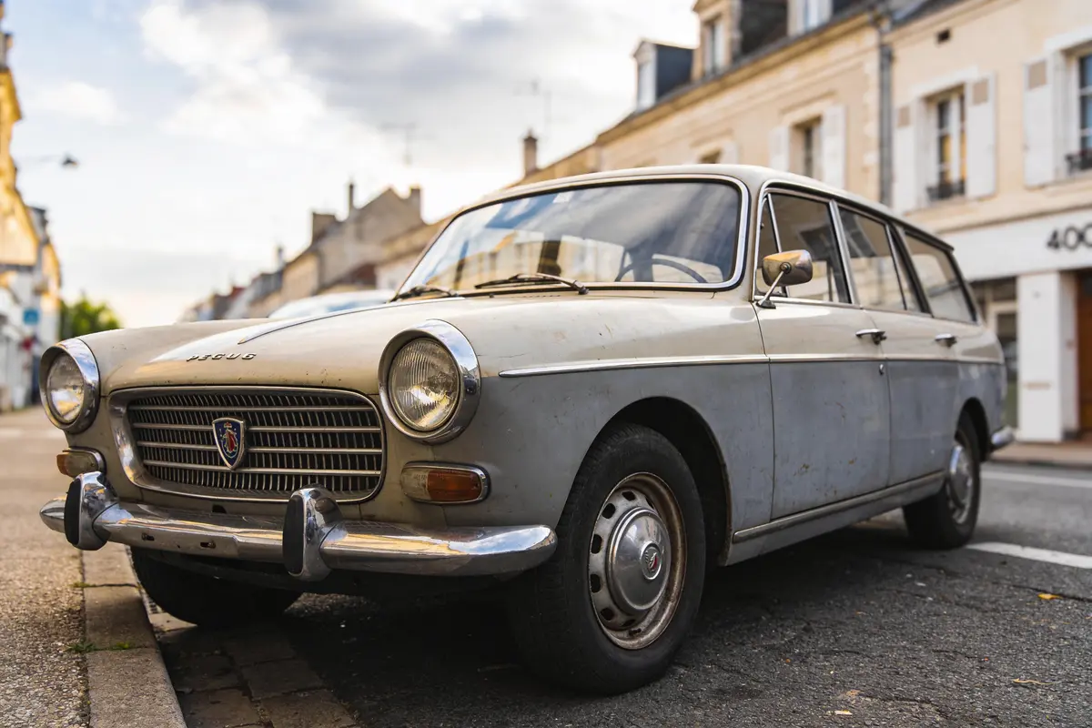 Voiture ancienne grise stationnée sur une rue pavée devant des bâtiments.