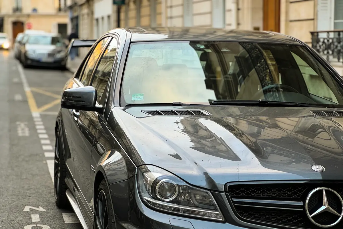 Voiture Mercedes grise garée dans une rue urbaine, bâtiments en arrière-plan.