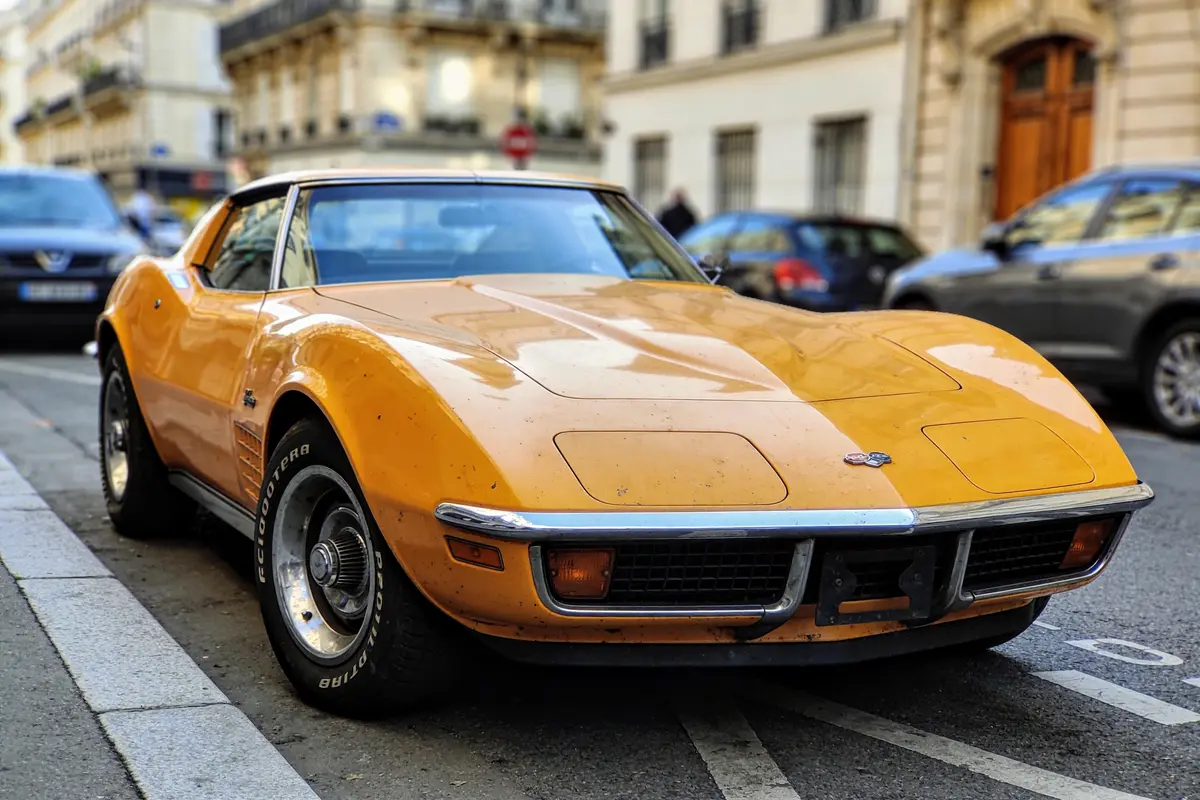 Voiture de sport vintage jaune garée dans une rue urbaine, entourée d'autres voitures et bâtiments.