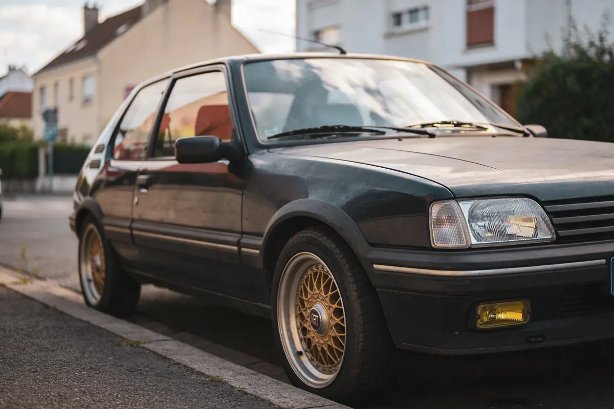 Voiture rétro noire stationnée dans une rue résidentielle, jantes dorées, maisons en arrière-plan.