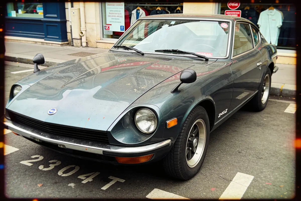 Voiture classique grise, modèle 240Z, stationnée en ville, vue de trois-quarts avant sur trottoir.