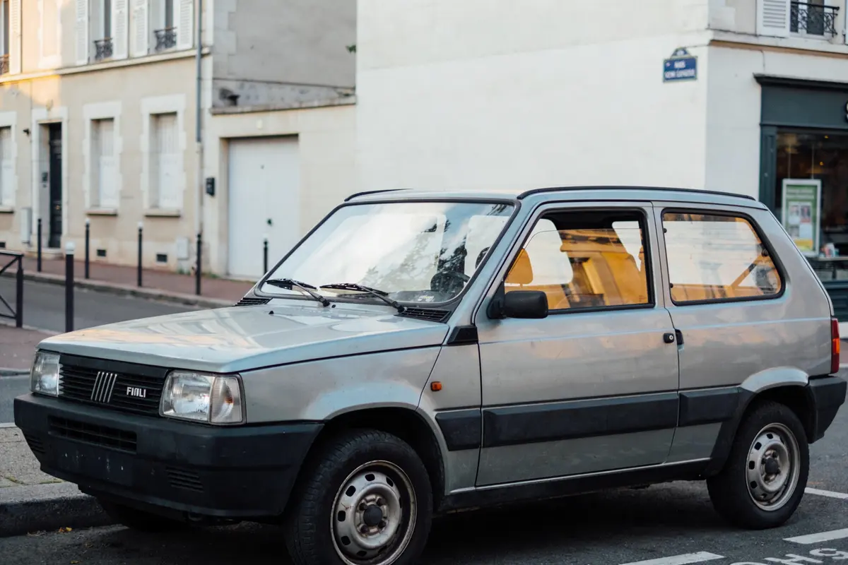 Voiture ancienne grise garée dans la rue devant bâtiments résidentiels clairs.