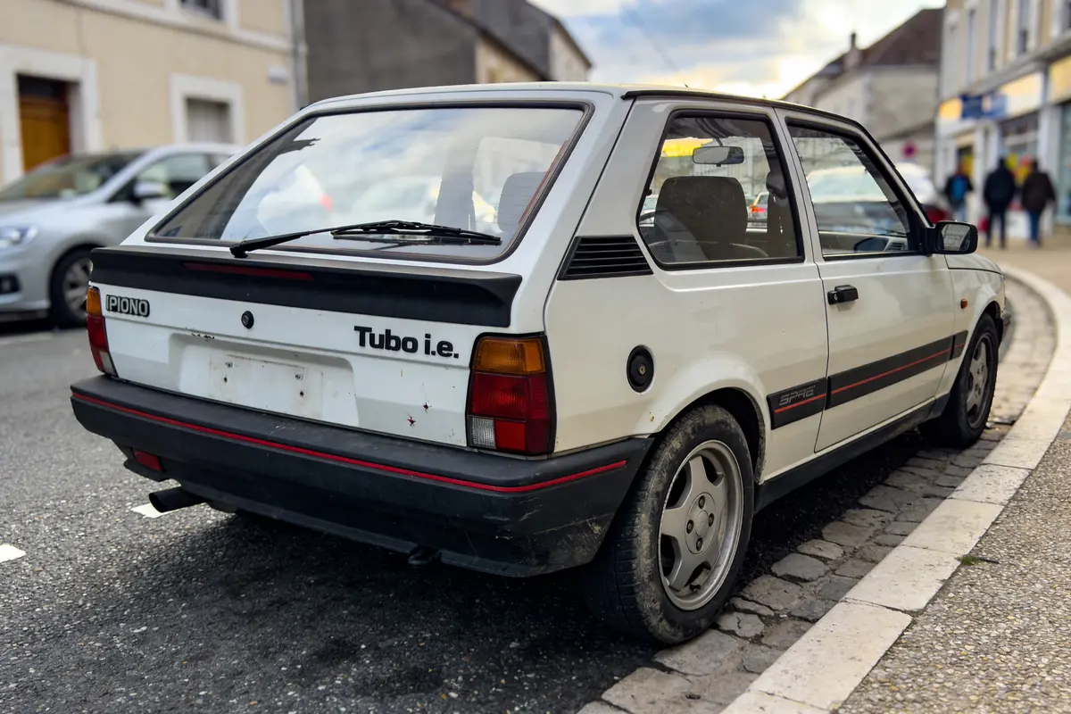 Voiture blanche rétro, modèle Turbo i.e, garée en ville sur un trottoir pavé.