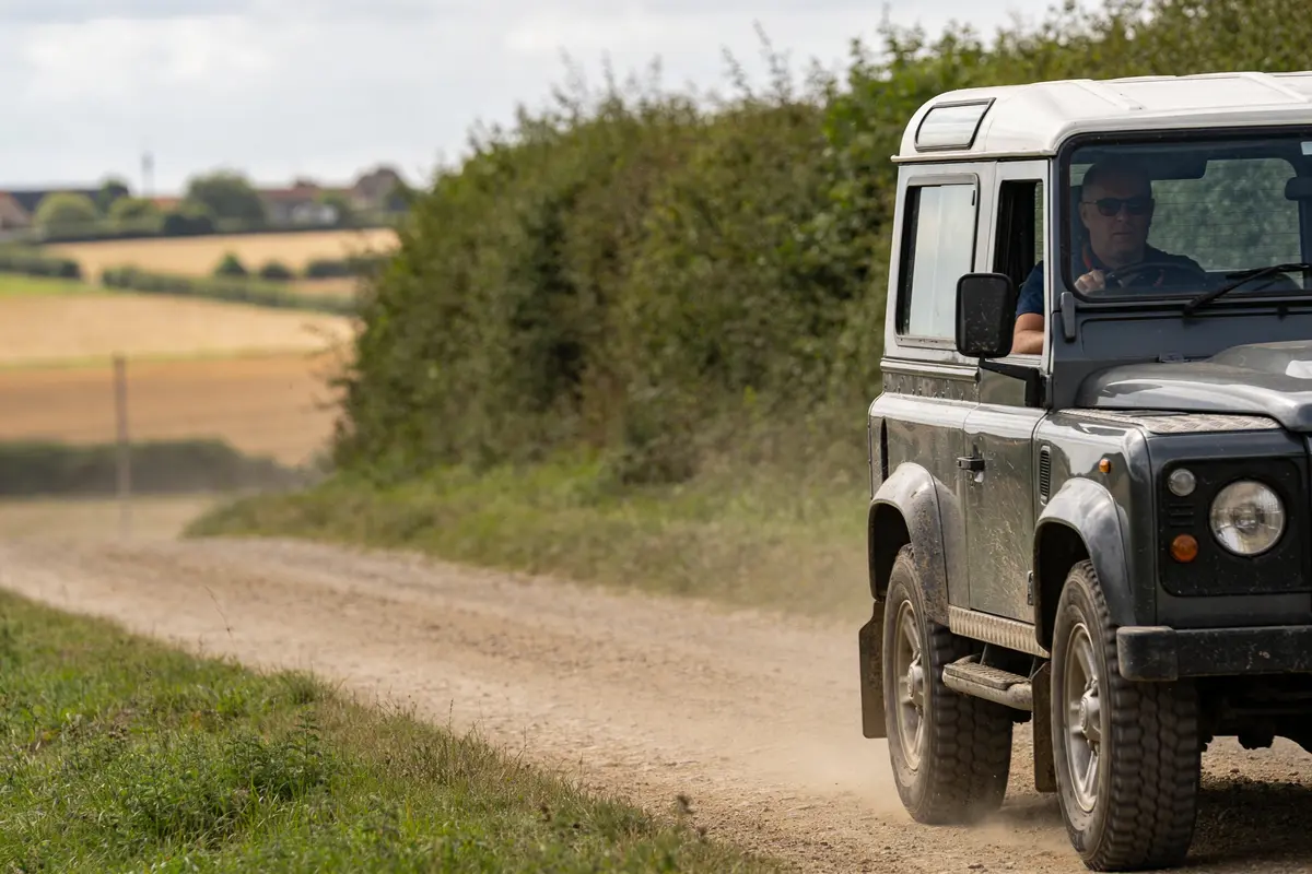 4x4 roulant sur chemin de terre, paysage de campagne avec champs en arrière-plan, conducteur porte des lunettes.