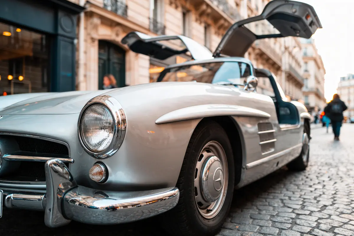 Voiture classique argentée avec portes papillon ouvertes, stationnée sur une rue pavée en ville.