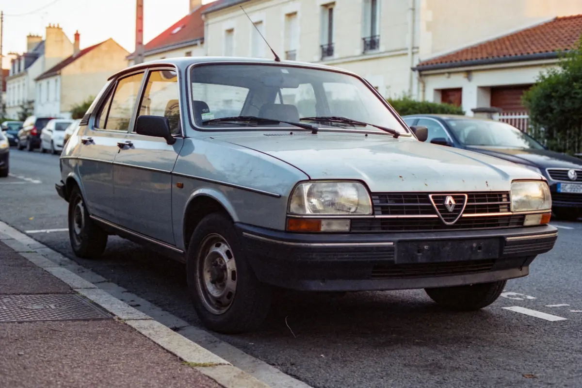 Vieille voiture grise Alfa Romeo garée dans une rue résidentielle bordée de maisons, par temps clair.