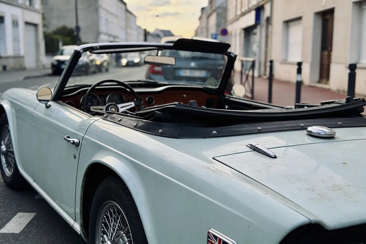 Voiture décapotable classique bleu pâle stationnée dans une rue bordée de bâtiments résidentiels au crépuscule.