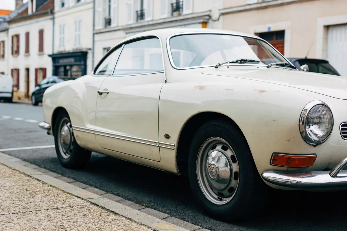 Voiture ancienne blanche stationnée dans une rue, devant des bâtiments traditionnels en arrière-plan.