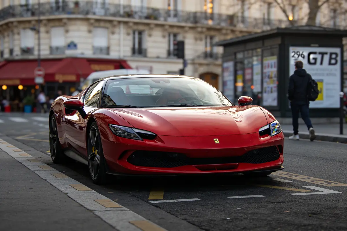 Voiture de sport rouge garée sur rue urbaine, immeuble et passant en arrière-plan.