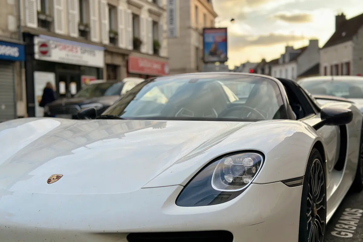 Voiture de sport blanche garée en ville, devant bâtiments et ciel nuageux.