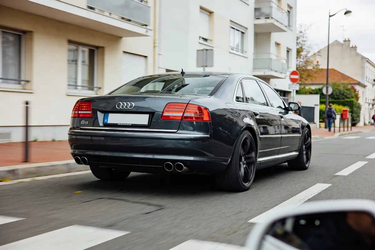 Voiture noire Audi A8 sur une rue urbaine, bâtiments résidentiels en arrière-plan.