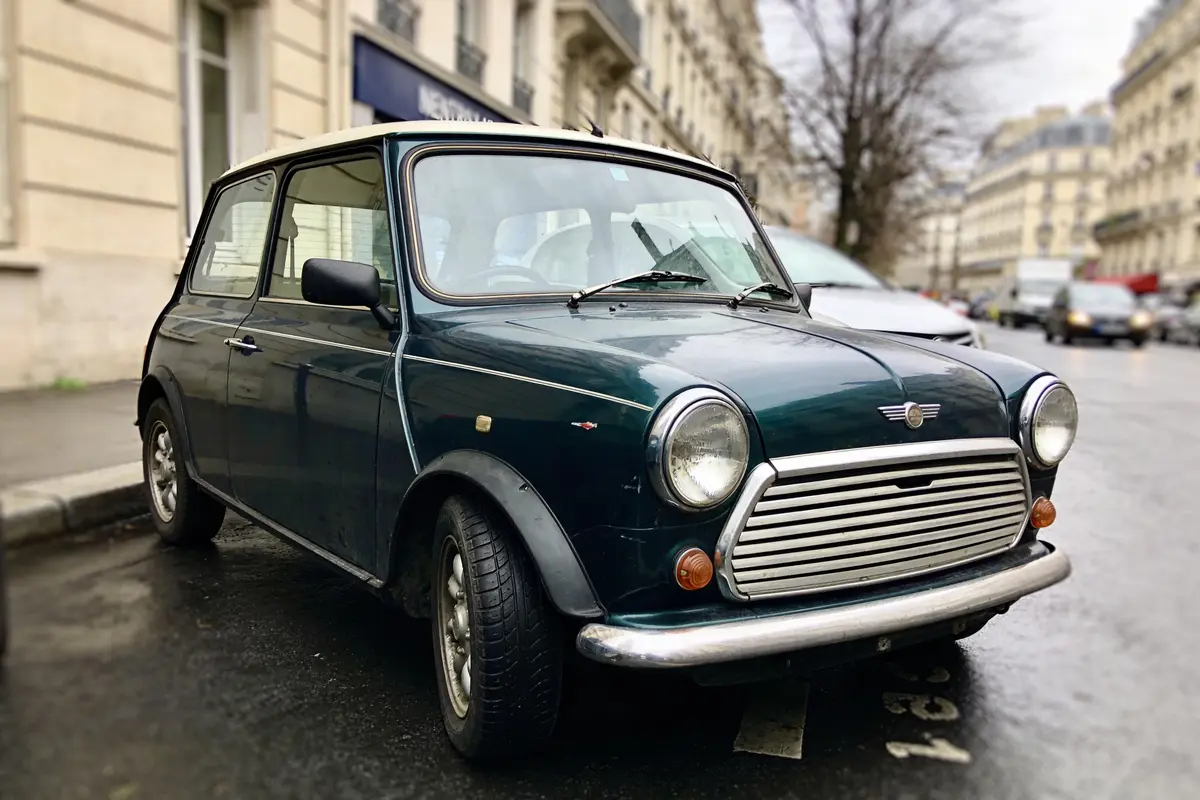 Petite voiture vintage verte garée sur une rue pavée, bâtiments parisiens en arrière-plan.