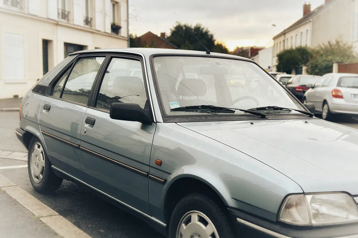 Voiture grise stationnée dans la rue, devant bâtiments résidentiels et d'autres véhicules.