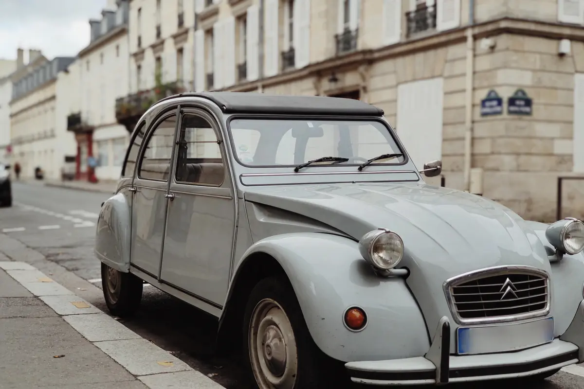 Voiture Citroën 2CV grise garée dans une rue parisienne avec bâtiments anciens en arrière-plan.