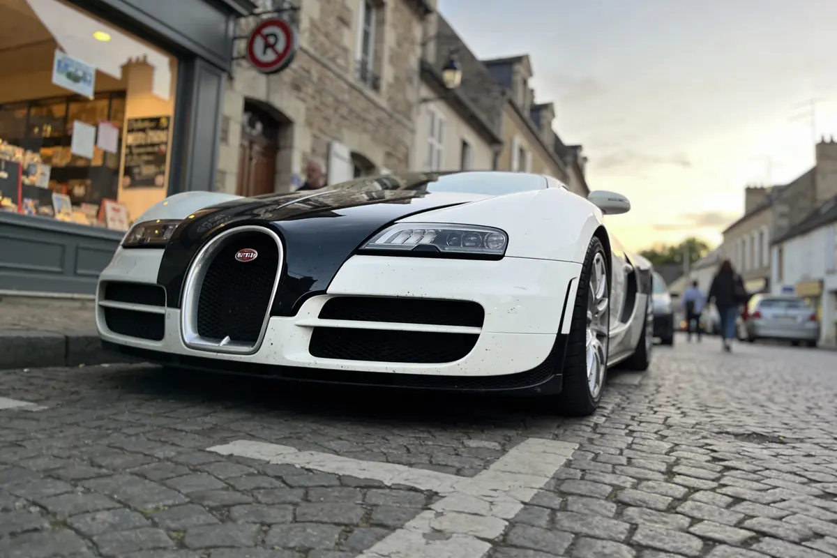 Voiture de sport blanche garée sur une rue pavée devant une boutique.