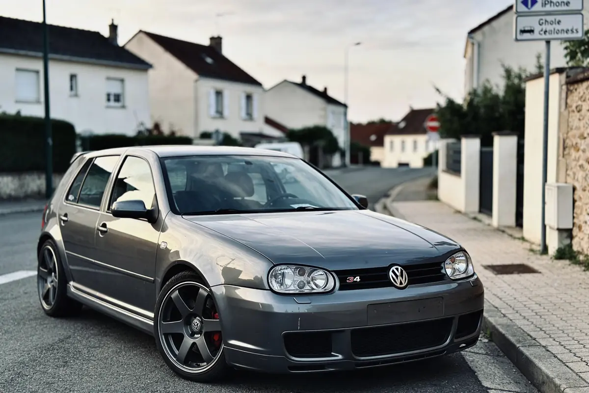 Voiture Volkswagen grise stationnée dans une rue résidentielle, maisons en arrière-plan, ciel légèrement nuageux.