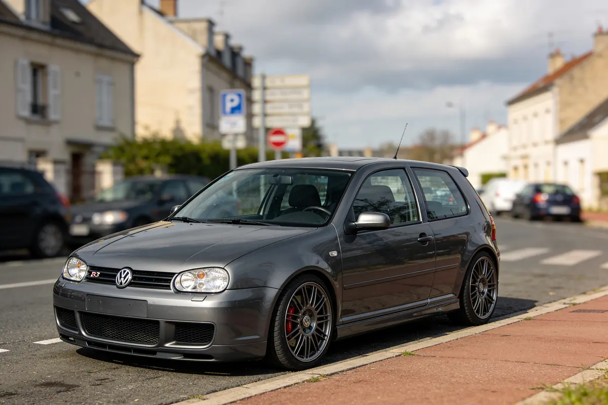 Voiture Volkswagen grise garée dans une rue résidentielle, avec d'autres voitures en arrière-plan.