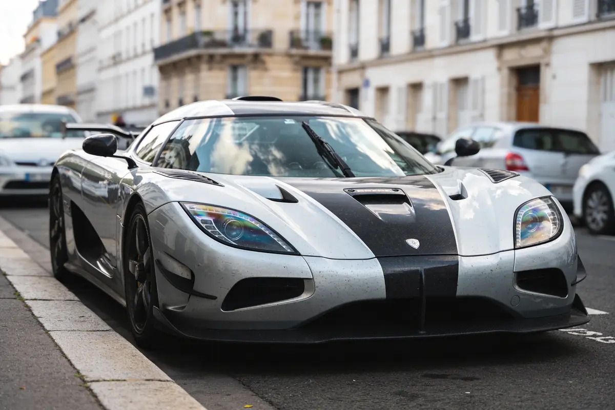 Voiture de sport argentée garée dans la rue urbaine, bâtiments flous en arrière-plan.