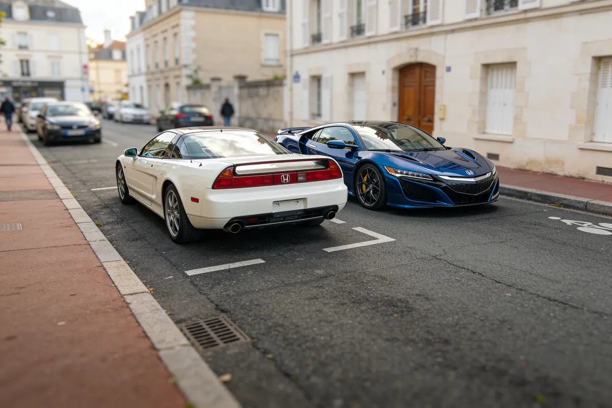 Deux voitures de sport, une blanche et une bleue, garées dans une rue résidentielle calme.