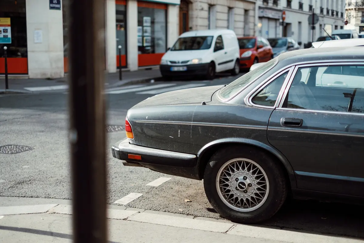 Voiture ancienne stationnée en ville, avec bâtiments et véhicules en arrière-plan. Propice à une scène urbaine typique.