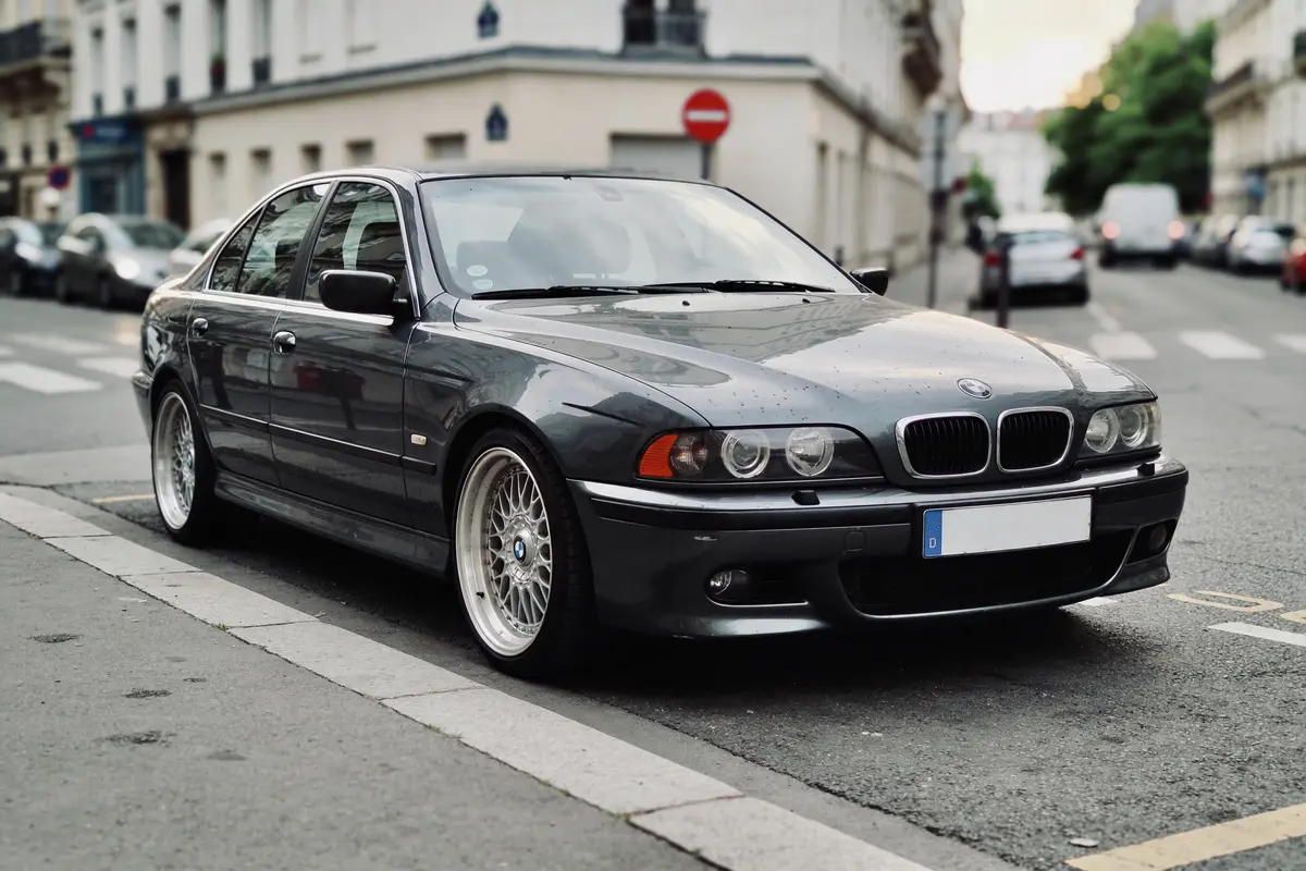 Voiture BMW grise garée dans une rue urbaine, bâtiments et autres voitures en arrière-plan.