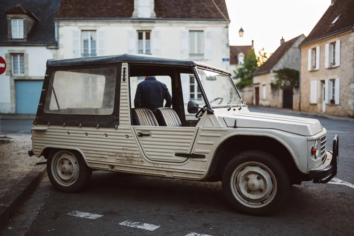 Voiture vintage blanche garée dans une rue avec des bâtiments en arrière-plan.