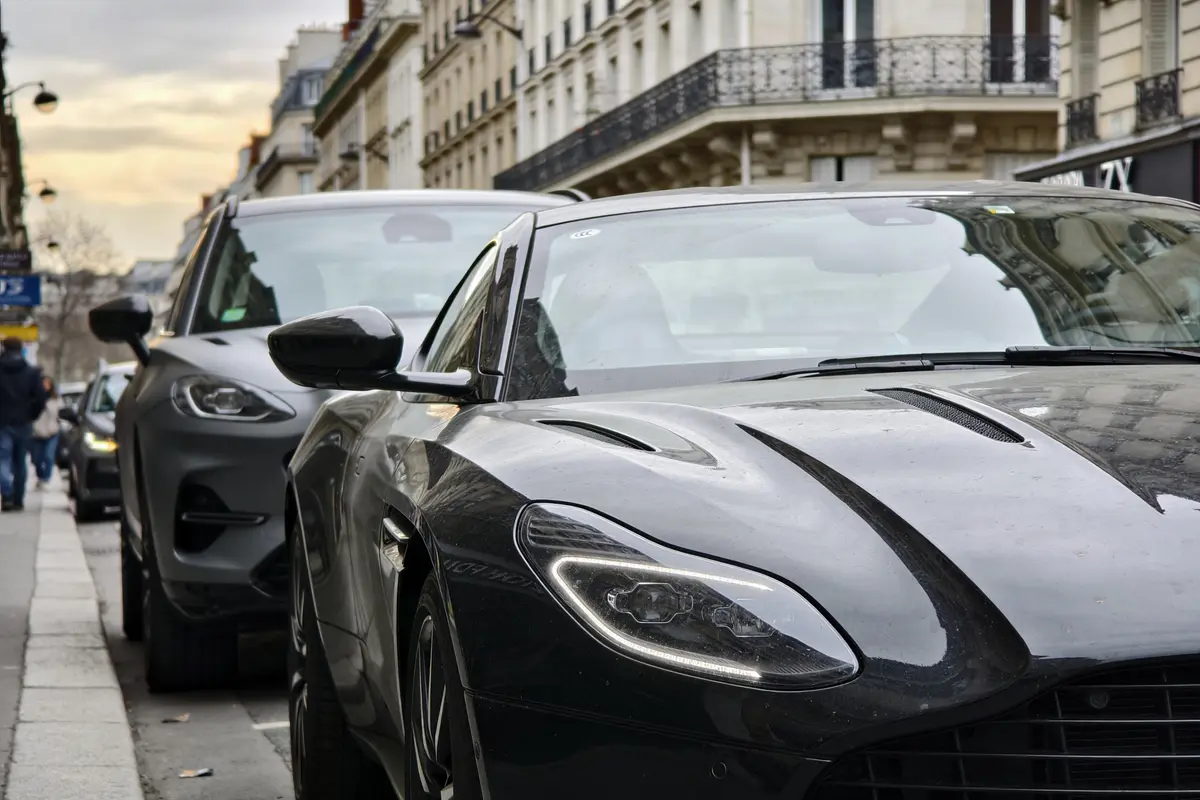 Voitures de luxe noires garées en enfilade dans une rue de ville. Immeubles en arrière-plan.