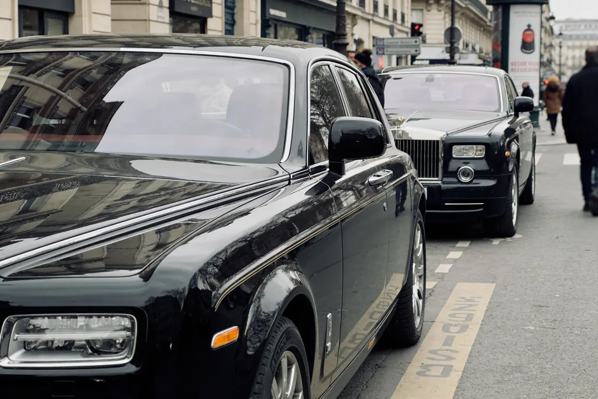 Deux Rolls Royce noires garées sur une rue urbaine avec plusieurs piétons en arrière-plan.