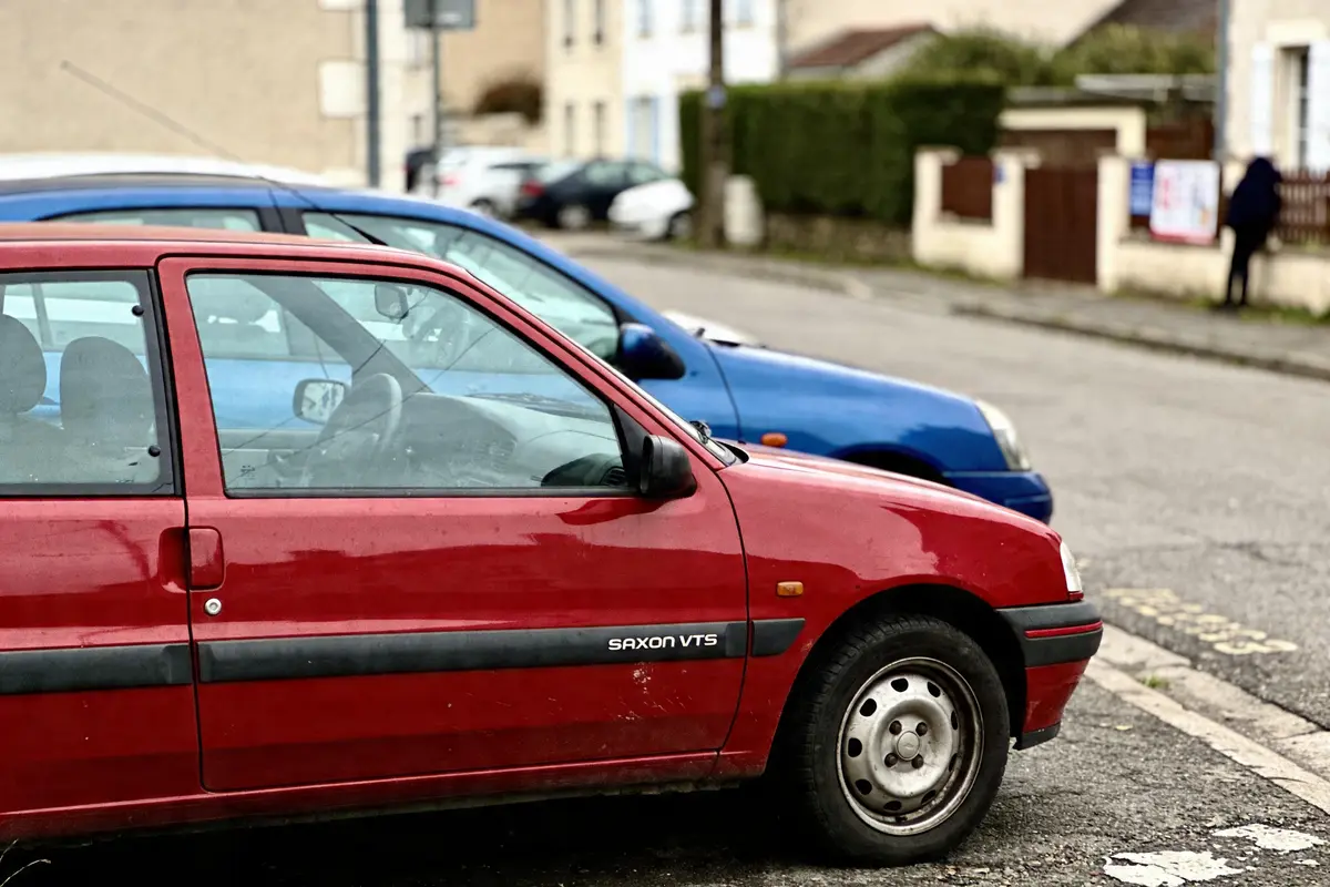 Voitures rouges et bleues garées dans une rue résidentielle, maisons en arrière-plan flou.