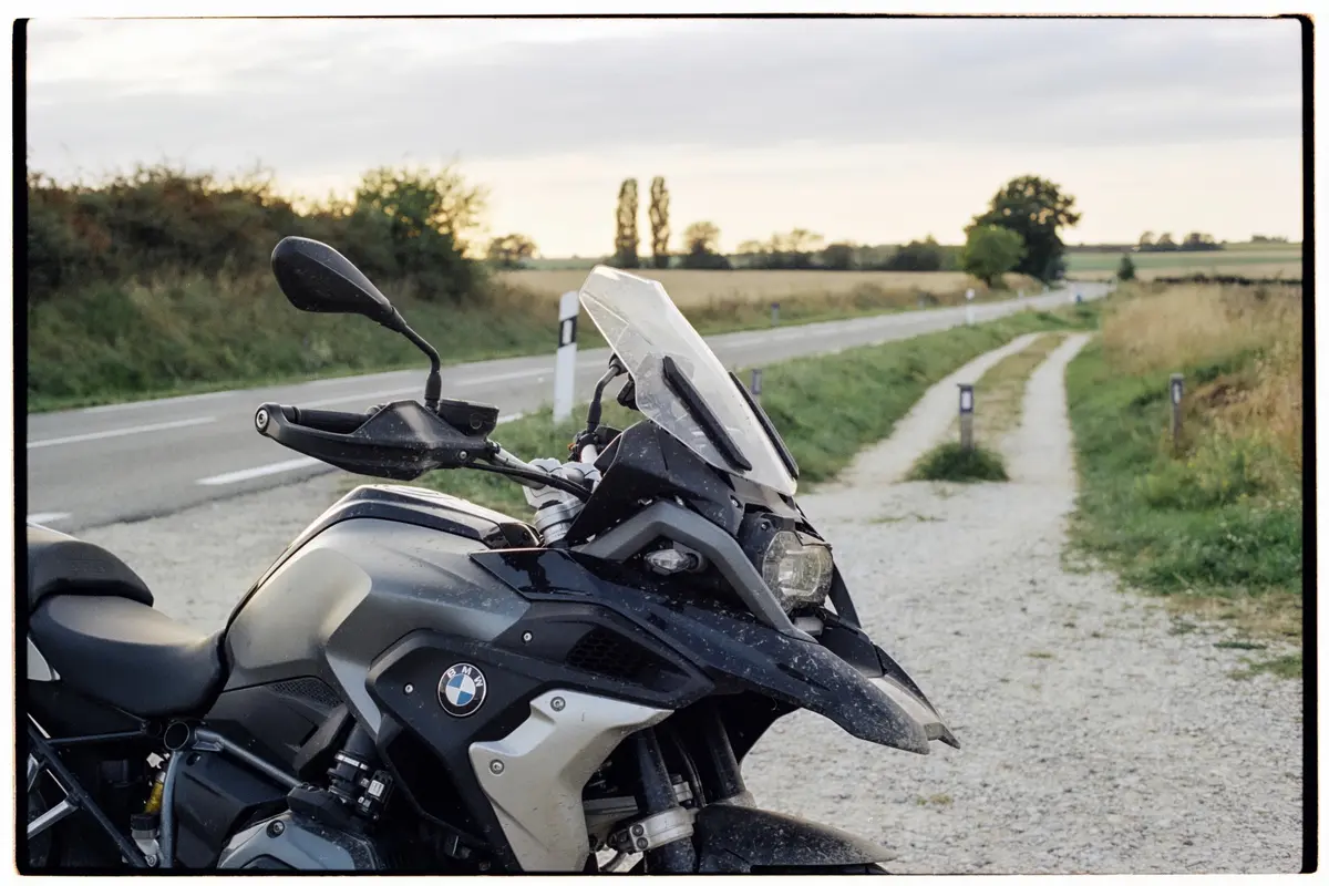 Moto stationnée près d'une route de campagne, ciel partiellement couvert, paysage verdoyant en arrière-plan.
