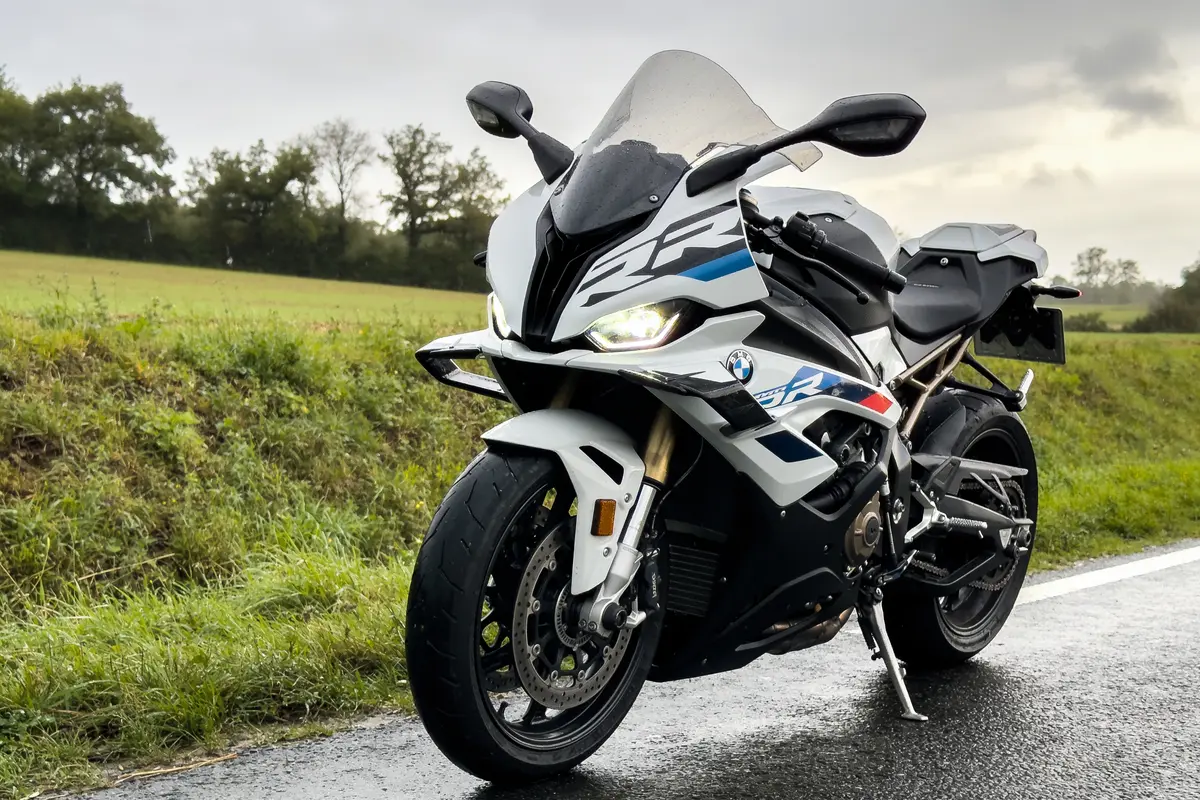 Moto sportive blanche stationnée sur une route mouillée, ciel nuageux et paysage verdoyant à l'arrière-plan.