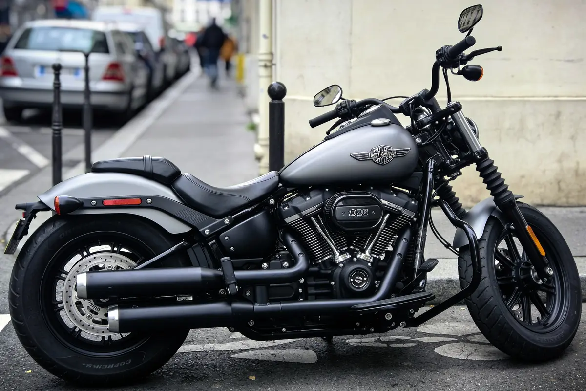 Moto grise stationnée en ville, modèle custom, détails noirs, rue en arrière-plan, voitures garées.