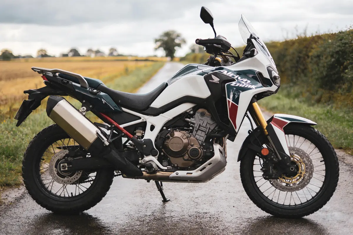 Moto Honda Africa Twin stationnée sur une route de campagne, ciel nuageux, champs en arrière-plan.