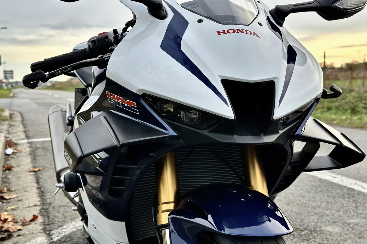 Moto sportive Honda blanche et bleue, route en arrière-plan, logos Honda et HRC visibles.