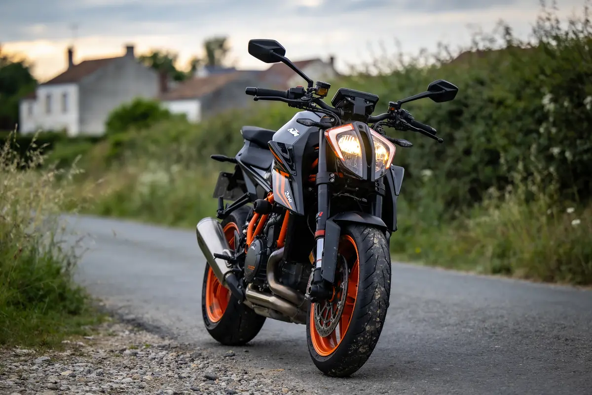 Moto noire et orange garée sur une route de campagne, maisons en arrière-plan.
