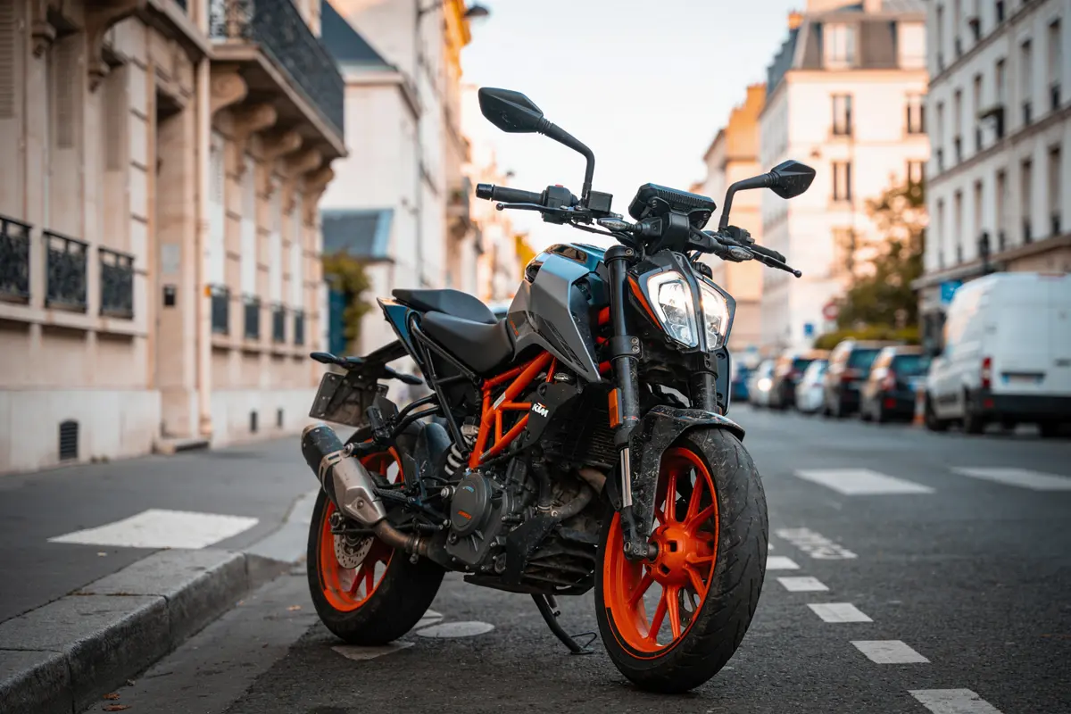 Moto noire et orange garée dans une rue urbaine bordée de bâtiments résidentiels.